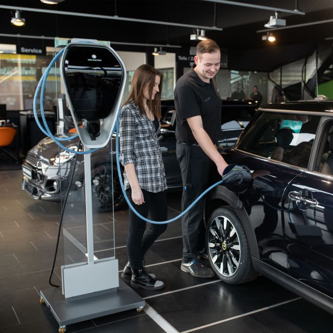 Servicemitarbeiter zeigt Kundin das Aufladen eines Minis